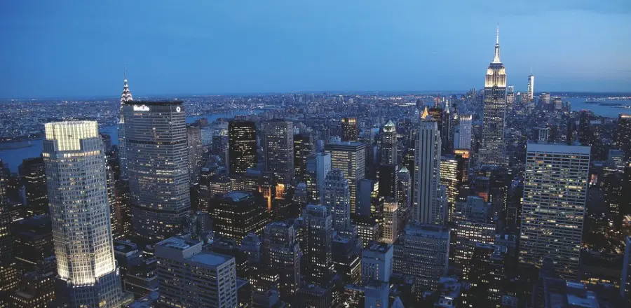 A shot of the Manhattan skyline at night, with bright lit buildings and a dark blue sky.
