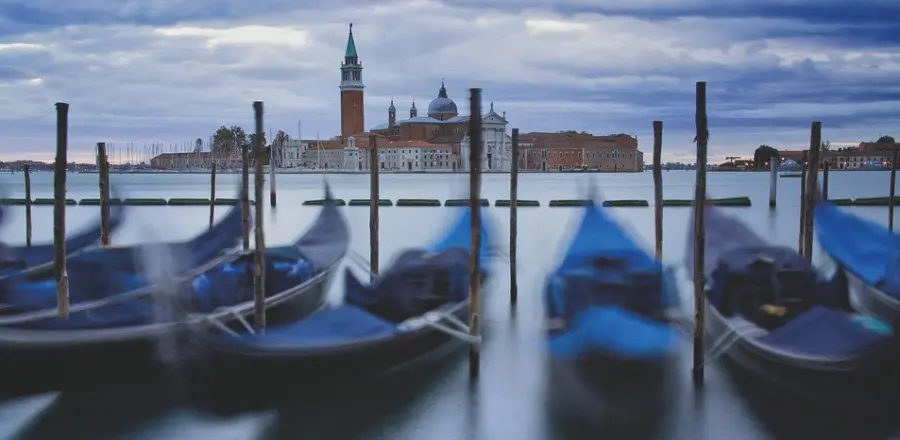 A shot of the venice harbor, with blue gondolas at the foreground and a red building in the background.