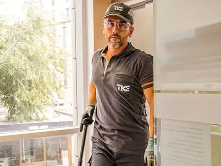  Ein TKE-Techniker im Arbeits-Polo-Shirt und einer schwarzen Baseballkappe mit dem TKE-Logo betritt einen Innenraum. 