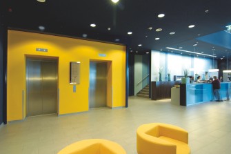 A modern elevator lobby with yellow accent walls and furniture. 