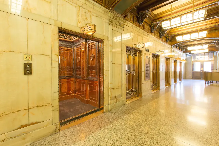 An elevator bank with marble walls featuring elevators with hardwood interior walls.