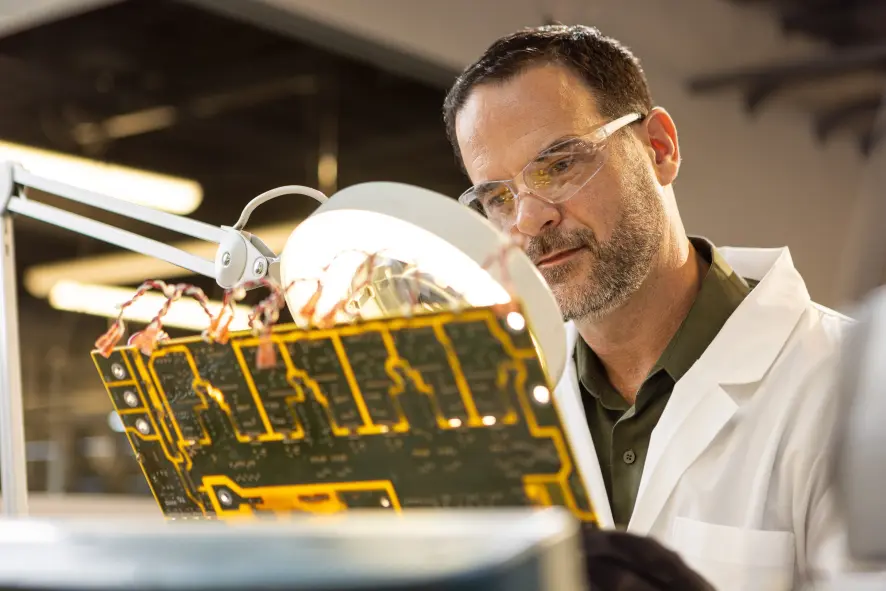 An engineer inspects a board through a magnifying lens.
