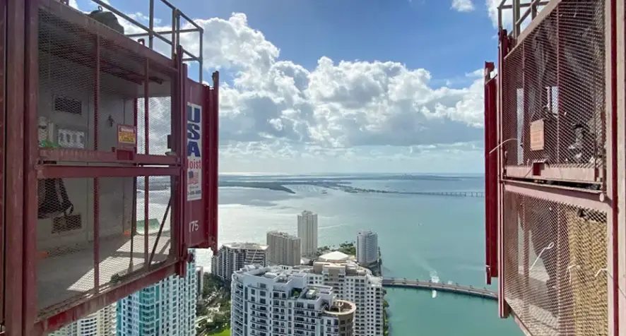 A photo taken from the high raised buck hoist elevator showing tall buildings and sea surrounding them.