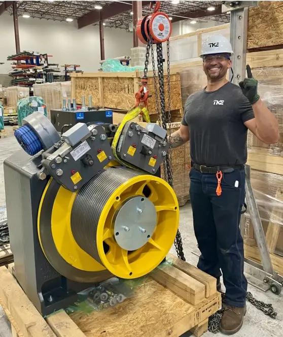 Ed Rivera standing next to a piece of machinery wearing a TK Elevator t-shirt.