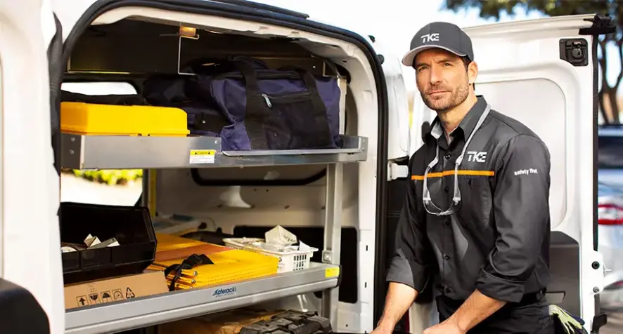A tech standing next to a work truck in a TK Elevator uniform