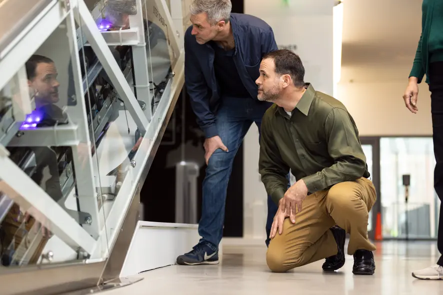 Two men investigating the inner workings of an escalator at the TK Elevator IQC.