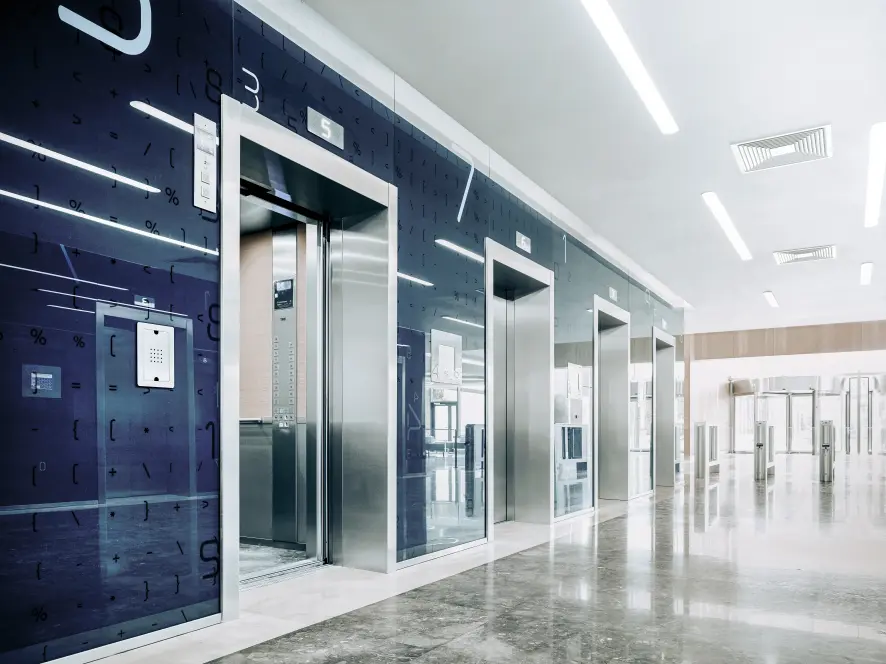 An elevator bank with complex outer walls complemented by simple elevator cab interiors.