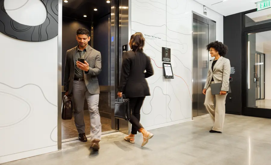 
A group of businesspeople enter and exit a TK Elevator high-rise elevator.
